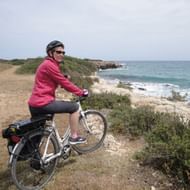 Velofahrerin steht an einer Klippe und betrachtet das Meer. Sizilien Südost. Veloferien mit Eurotrek.