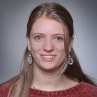 Professionelles Portrait von Elisa Simonazzi mit langen blonden Haaren, trägt dekorative Ohrringe und einen roten Strickpullover.