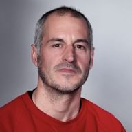 Porträt von Pablo Bachiller in einem roten Shirt vor hellgrauem Hintergrund. Er hat kurzes graues Haar und einen Bart.