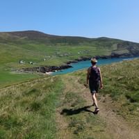Eine Wandererin vor einer Bucht im Hintergrund grüne Hügel