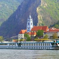 Navire de croisière fluviale blanc MS Katharina sur le Danube devant le monastère historique de Dürnstein avec tour baroque bleue et toits rouges.