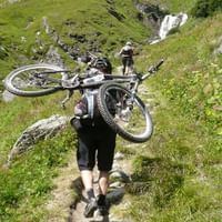 Personne forte qui porte le vélo sur ses épaules. Vélo alpin. Vacances à vélo avec Eurotrek.