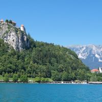 Burg Bled thront auf einem Felsen über dem türkisfarbenen Bleder See in Slowenien, mit schneebedeckten Alpen im Hintergrund und einer Kirche.