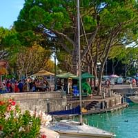 Jetée en pierre avec bateaux amarrés dans l'eau turquoise à Sirmione sur le lac de Garde. Des foules de touristes se promènent le long de la promenade.