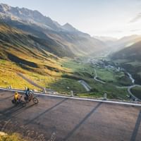 Zwei Velofahrer fahren eine Passstrasse hoch. Im Hintergrund die Bergwelt Graubündens.