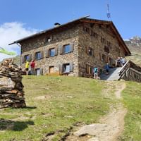 Ein Wanderer steht vor einer Hütte und schaut in Richtung der Berggipfel.
