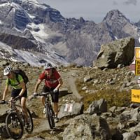 Zwei Mountainbiker in den Alpen. Ein Wegweiser zeigt ihnen die weitere Route zum Kesch in den Bündner Bergen.