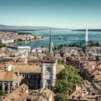 Blick von oben auf die Altstadt Genf mit dem See und der Fontäne im Hintergrund.