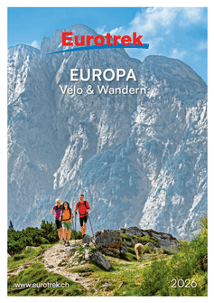 Titelbild des Eurotrek 2026 Katalogs mit drei Wanderern mit Rucksäcken auf einem felsigen Bergpfad vor dramatischen Alpengipfeln.