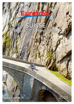 Couverture du catalogue Eurotrek 2026 montrant deux cyclistes sur un pont de pierre traversant des gorges rocheuses en Suisse avec mousse verte.