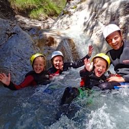 Vier Personen in Neoprenanzügen und Helmen beim Canyoning in einem felsigen Bach in Tirol, mit fließendem Wasser und natürlichen Felsformationen.