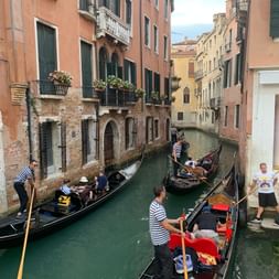 Durch einen kleinen Kanal in Venedig fahren zwei Gondoliere aneinander vorbei.