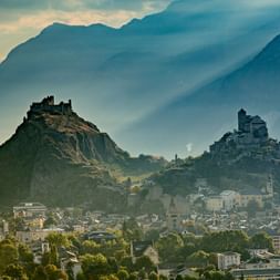 Two mountain peaks with an old and an intact castle. Down in the valley is Sion.
