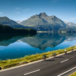 Velofahrer fahren auf einer Strasse vor dem Maloja See im Graunbünden.