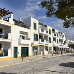Reihe weißer Häuser mit gelben Akzenten und grünen Fensterläden entlang einer Kopfsteinpflasterstraße in Cacela Velha, Algarve.