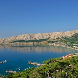 Luftaufnahme der Stadt Baska auf der Insel Krk mit blauer Adria, weißen Kalksteinklippen, Marina und mediterraner Vegetation.