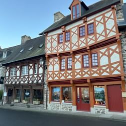 Traditionelle Fachwerkhäuser in Tréguier, Bretagne, mit orangebraunen Holzbalken und weißem Putz. Das Hauptgebäude hat drei Stockwerke.