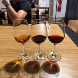 Drei Weingläser auf einem Holztisch zeigen Ruby-, Tawny- und weißen Portwein während einer Degustation in Porto.