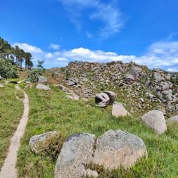 Schmaler Wanderweg durch Granitfelsen-Landschaft im Peneda-Gerês-Nationalpark, Portugal, mit grünem Gras und blauem Himmel.