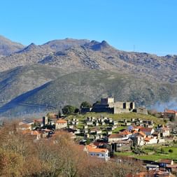 Mittelalterliche Burg Lindoso auf Hügel über Dorf mit roten Ziegeldächern im Peneda-Gerês-Nationalpark, umgeben von Bergen.