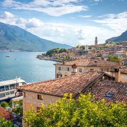 Malerischer Blick auf Limone sul Garda mit bunten Gebäuden entlang der Gardasee-Küste, Bergen im Hintergrund und einem Touristenboot im Wasser.