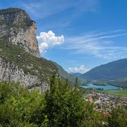 Panoramablick auf den Tobliner See umgeben von Bergen und einem Dorf. Felsige Klippen mit Vegetation rahmen den türkisfarbenen See unter blauem Himmel.