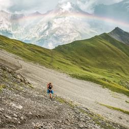 Ein Wanderer steht auf dem Alpschelegrat über Kandersteg. Über die Bergspitzen strahlt ein Regenbogen.