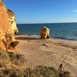 Sandstrand in Portimão mit goldenen Klippen und einer großen Felsformation im ruhigen blauen Meer unter klarem Himmel.
