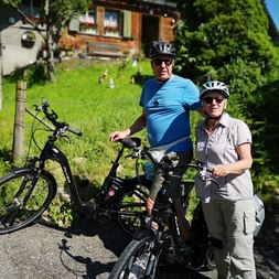 Zwei Radfahrer posieren vor einem traditionellen Haus auf ihrer Radtour.