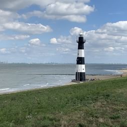 Sicht auf einen schwarz-weiss gestreiften Leuchtturm am Strand.