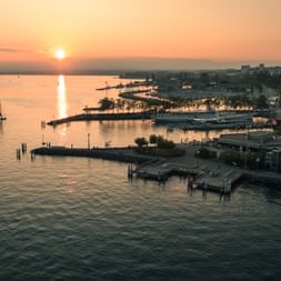Vue aérienne du port de Lausanne au coucher du soleil avec la lumière dorée se reflétant sur le lac Léman. Des voiliers et la marina sont visibles.