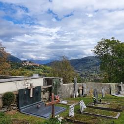 Foto von einem Friedhof. Im Hintergrund sieht man ein Dorf und einen Wald. Sentiero Lago di Lugano. Wanderferien mit Eurotrek.
