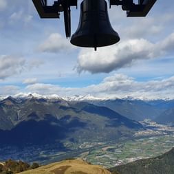 Weite Sicht über viele Berge. Am oberen Rand sieht man eine Glocke. Sentiero Lago di Lugano. Wanderferien mit Eurotrek.
