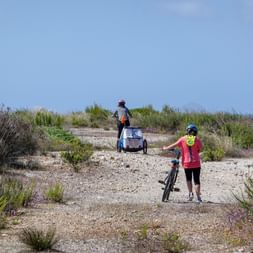 Zwei Radfahrer mit einem Kinderanhänger an einem Strandabschnitt auf Sardinien