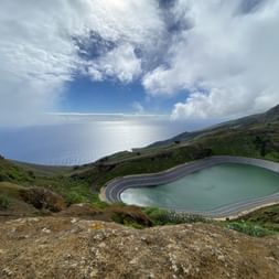 Der Stausee von El Hierro glänzt blau während im Hintergrund das Meer zu sehen ist.