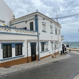 Weiße portugiesische Häuser mit blauen Verzierungen an einer Küstenstraße in der Algarve. Die Gebäude blicken aufs Meer mit Promenade und Strand.