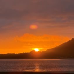 Dramatischer Sonnenuntergang in Caminha mit orangefarbenem und violettem Himmel. Die Sonne geht hinter einer dunklen Hügelsilhouette unter.