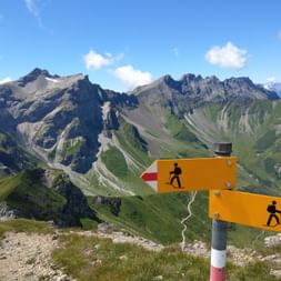 Un panneau indicateur de randonnée se trouve devant un décor de montagnes verdoyantes au Liechtenstein.