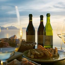 Zwei Weingläser stehen auf einem Tisch in einem Restaurant mit Ausblick auf einen See.