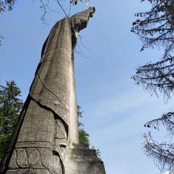 Hohe Steinstatue des Christkönigs von unten betrachtet, umgeben von Baumzweigen vor blauem Himmel nahe Mont Blanc.