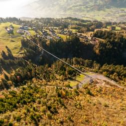 Aerial view of Lake Lucerne region with winding road through forests, green meadows, scattered houses, and mountain slopes in background.