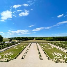 Vue aérienne des jardins à la française du Château de Chambord avec pelouses symétriques, motifs ornementaux et allées bordées d'arbres.