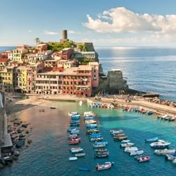 Luftaufnahme des Dorfes Vernazza in Cinque Terre mit bunten Häusern an Klippen, kleinem Hafen voller Boote und türkisfarbenem Mittelmeer.