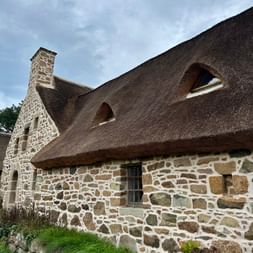 Steinhaus mit dickem Strohdach und Schornstein in Plougrescant, Bretagne. Die Mauern bestehen aus bunten Feldsteinen mit weißem Mörtel.