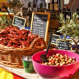 Étal de marché provençal coloré avec panier de tomates séchées, bols d'olives marinées, branches d'olivier et bouteilles d'huile d'olive.