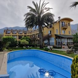 Pool mit Palme im Vordergrund und gelbes längliches Hotelgebäude im Hintergrund