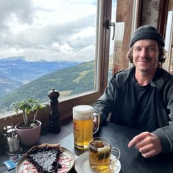 Stück Heidelbeertarte mit Puderzucker auf einem Teller im Hotel Weisshorn, mit Bergblick durch das Fenster.