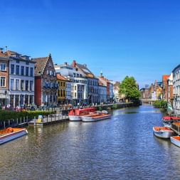 Kanal in Gent gesäumt von bunten historischen Gebäuden und Ausflugsbooten. Mittelalterliche Architektur mit Treppengiebeln spiegelt sich im Wasser.