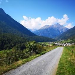 Naturstrasse zwischen Weideland, die direkt zum Dorf führt, welches unter den schönen Bergen liegt.