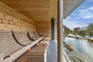 Moderner Sauna-Ruhebereich im Hotel Sand mit Holzliegen vor bodentiefen Fenstern mit Blick auf einen Außenpool und Bergpanorama.